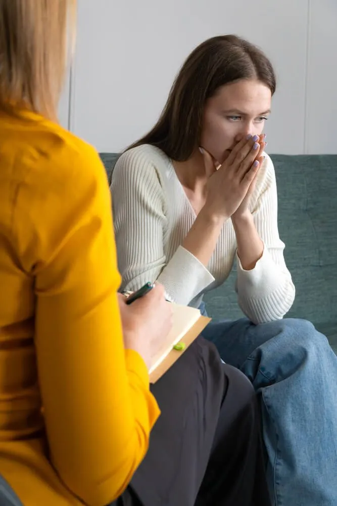 A woman speaking to a therapist with her hands pursed in front of her mouth